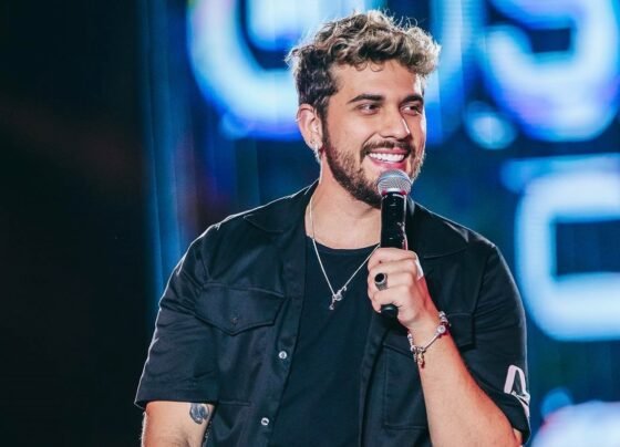 Cantor Gustavo Mioto sorrindo de perfil com microfone na mão - Metrópoles